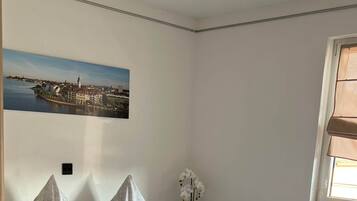 A bedroom with a bed, a nightstand, a window, and a wall-mounted picture.