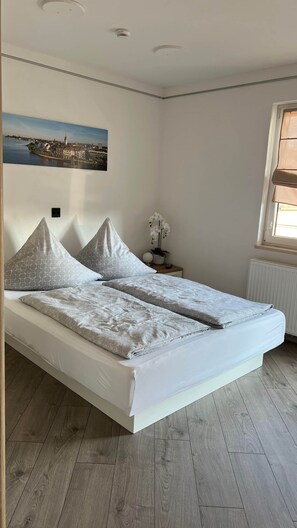 A bedroom with a bed, a nightstand, a window, and a wall-mounted picture. - David´s Apartment (Meckenbeuren)