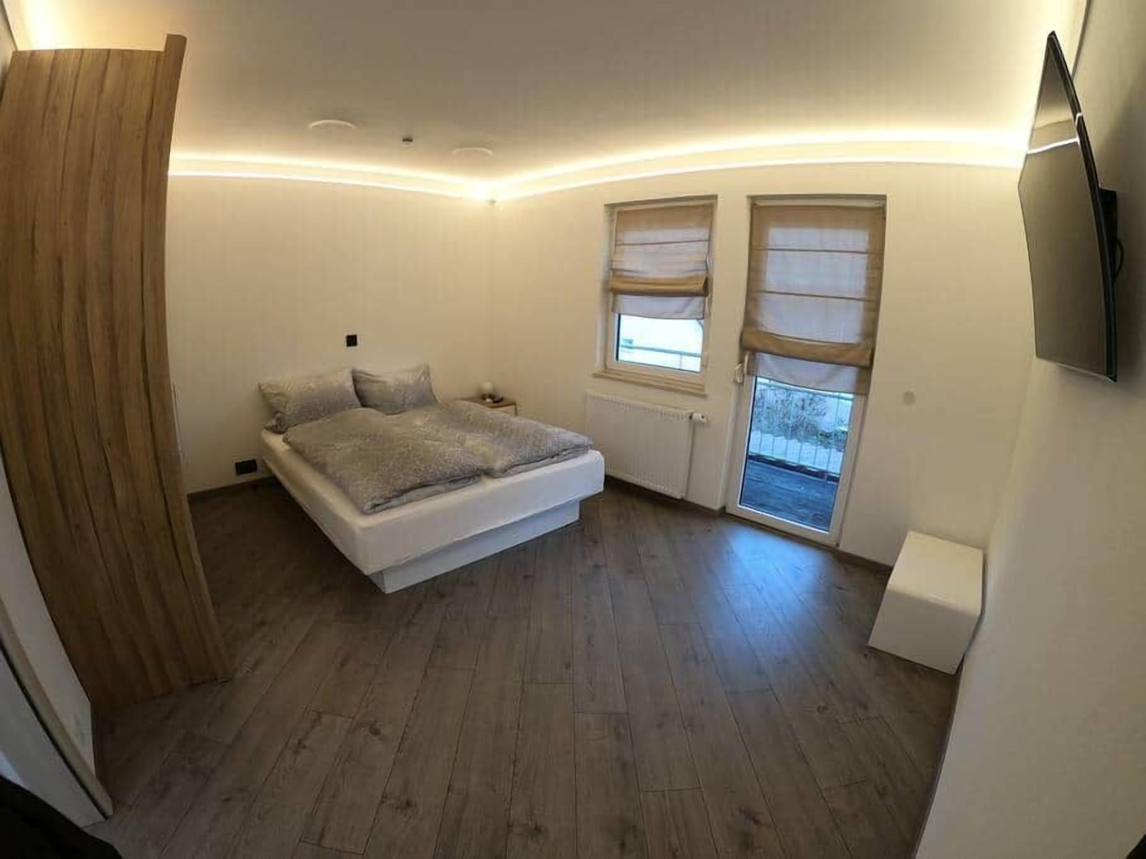 Een slaapkamer met een bed, een raam, een aan de muur bevestigde televisie en een deur.