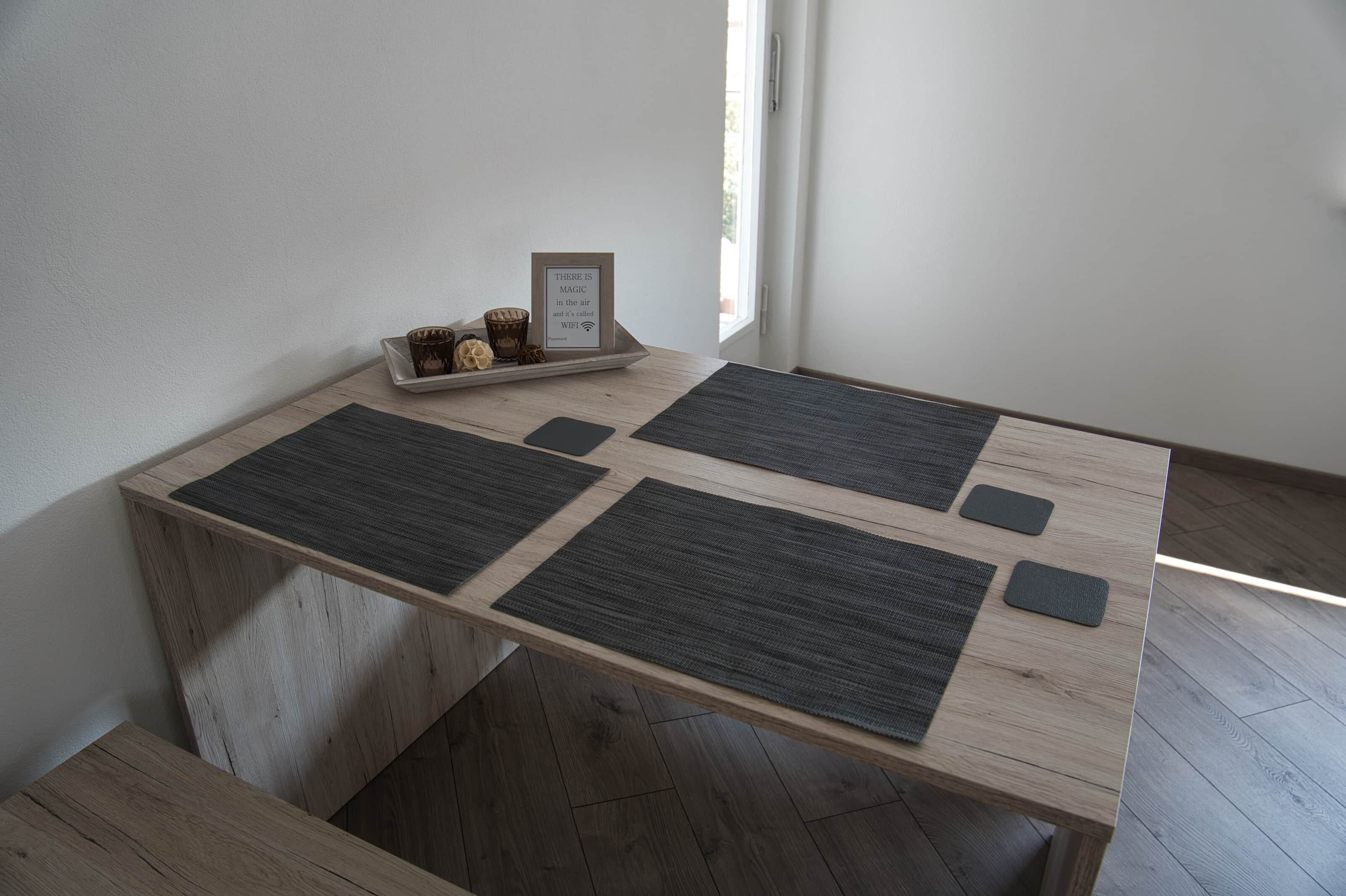 A wooden table with four dark mats and a tray with decorative items and a framed sign.