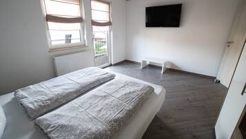 A bedroom with a bed, a radiator, a window with blinds, a television on the wall, and a door.