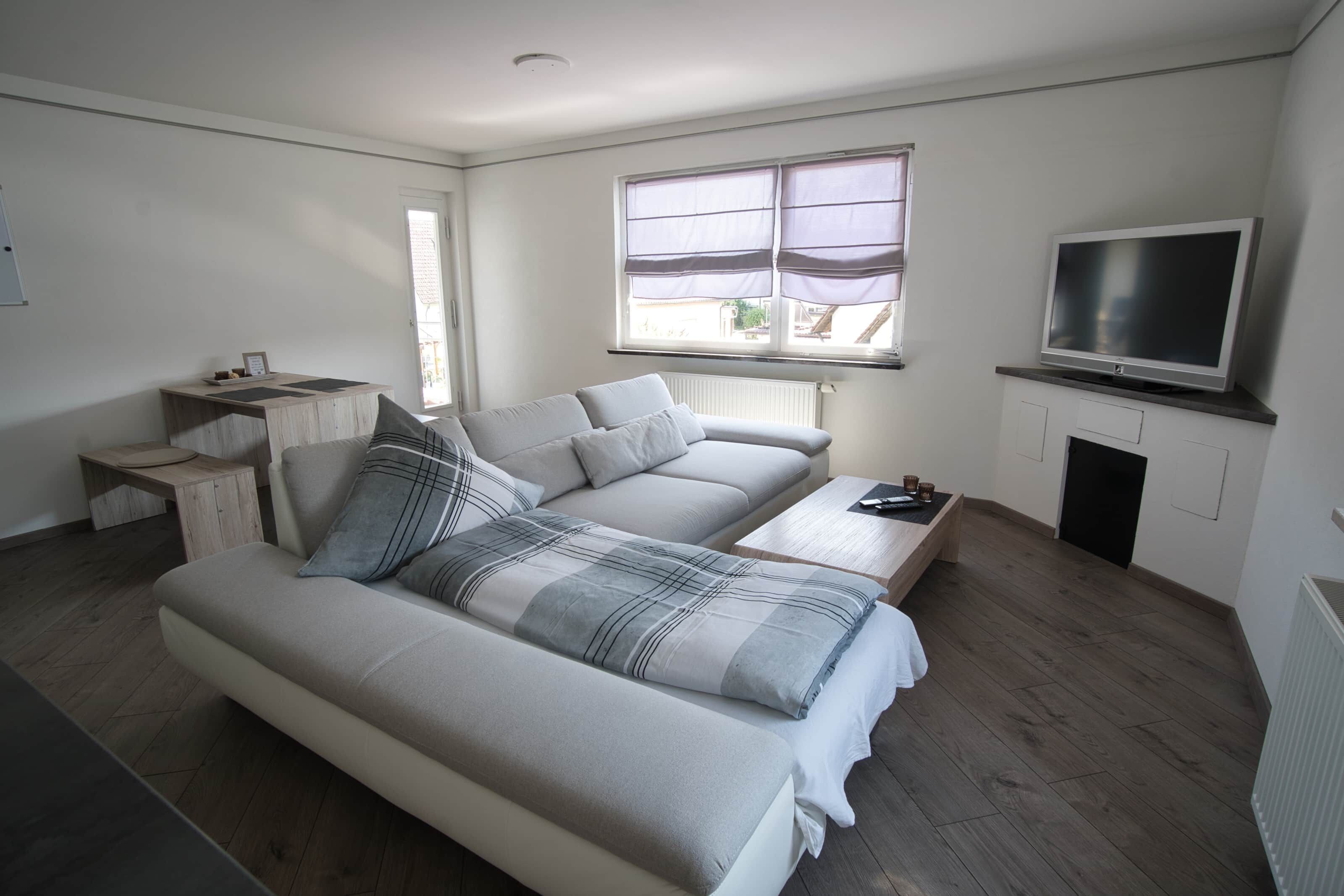 Ein modernes Schlafzimmer mit einem großen Bett, einem Fernseher, einem kleinen Tisch und einem Fenster mit Jalousien.