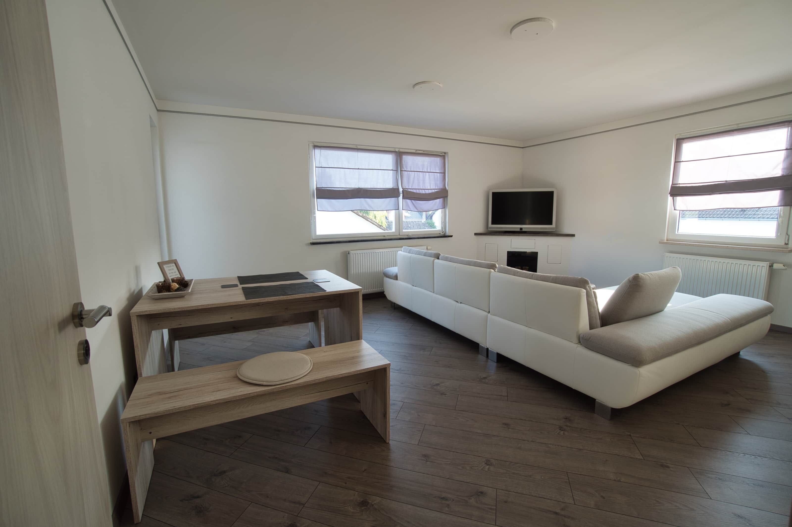 Ein modernes Wohnzimmer mit einer Couch, einem Fernseher und einem Esstisch mit einer Bank.