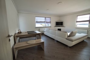 Un salon moderne avec un canapé, un téléviseur et une table à manger accompagnée d’un banc.