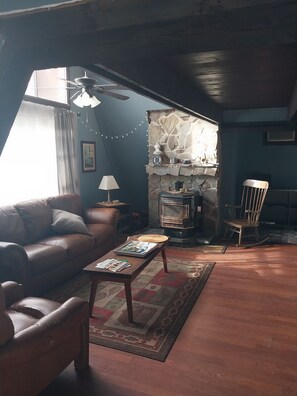 Ein gemütliches Wohnzimmer mit einem Ledersofa, einem Holztisch, einem Kamin aus Stein und einem Deckenventilator.