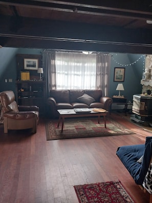A living room with a brown leather sofa, a wooden coffee table, and a blue sofa. There is a bookshelf with a lamp, a rug, and a window with curtains. - Beautiful 3-bedroom house in nice Dover perfect for your getaway (Dover)