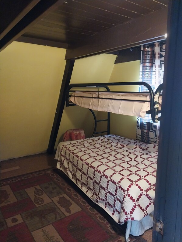 Ein Stockbett mit gemustertem Bettbezug, einem kleinen Teppich und einem Fenster mit Vorhängen.