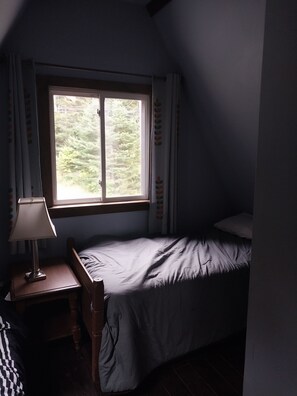 A small, dimly lit room with a single bed, a nightstand, and a window overlooking a forest. - Beautiful 3-bedroom house in nice Dover perfect for your getaway (Dover)