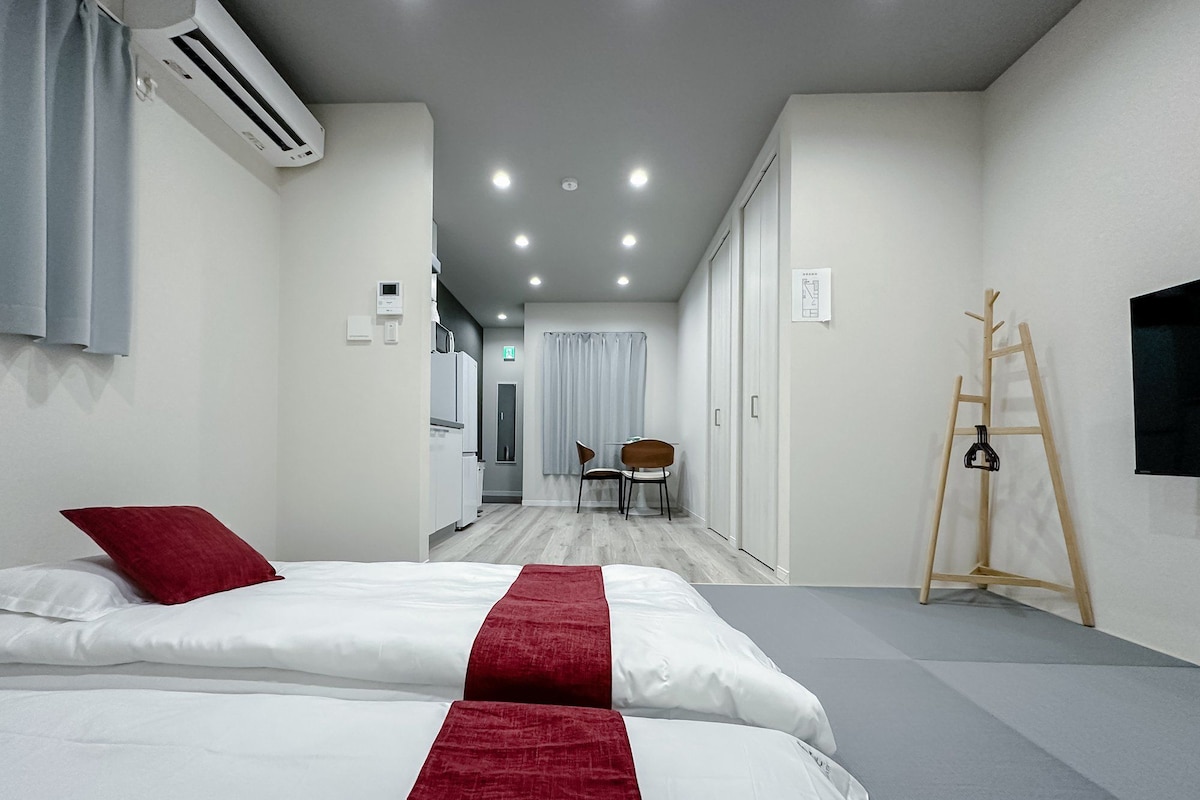 A hotel room with a bed, a desk, a chair, an air conditioning unit, and a television on the wall.