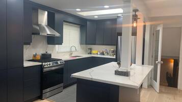 A modern kitchen with dark cabinets, a central island, a stove, and a window with blinds.