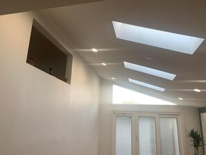 Habitació amb un fanal, llums integrades al sostre, una finestra amb persianes i una petita estant amb objectes decoratius.