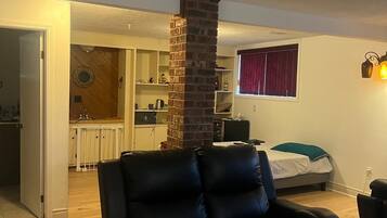 A living room with a black leather sofa, a brick fireplace, and a kitchen in the background.