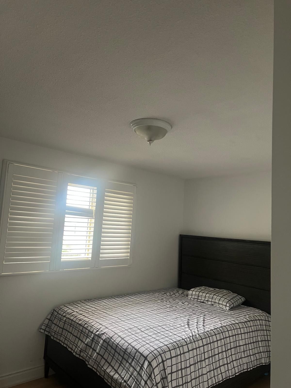 A bedroom with a bed, a window with blinds, and a ceiling light fixture.