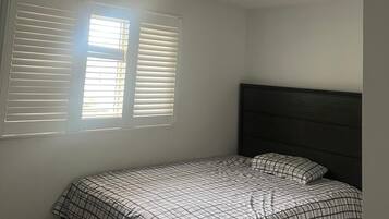 A bedroom with a bed, a window with blinds, and a ceiling light fixture.