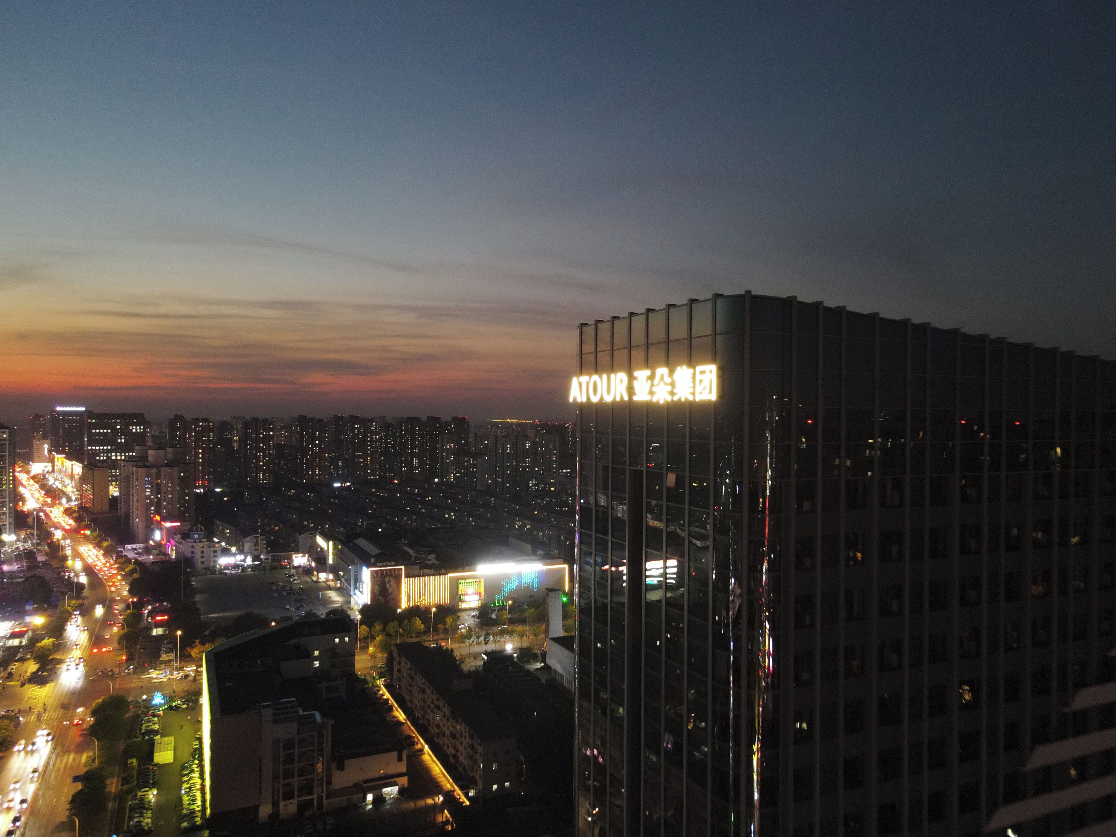 A high-rise building with illuminated signage, surrounded by a cityscape at dusk.