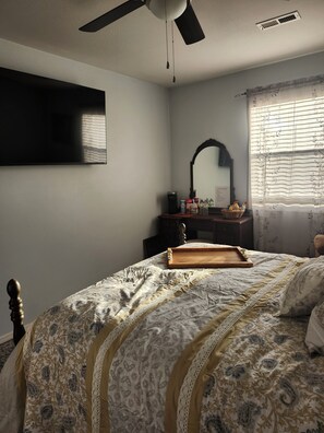 Un dormitorio con cama, cómoda, espejo y ventana con cortinas.