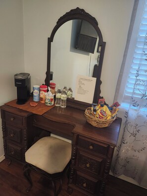 Un escritorio de madera con un espejo, una cafetera y diversos objetos, incluyendo una cesta de aperitivos.