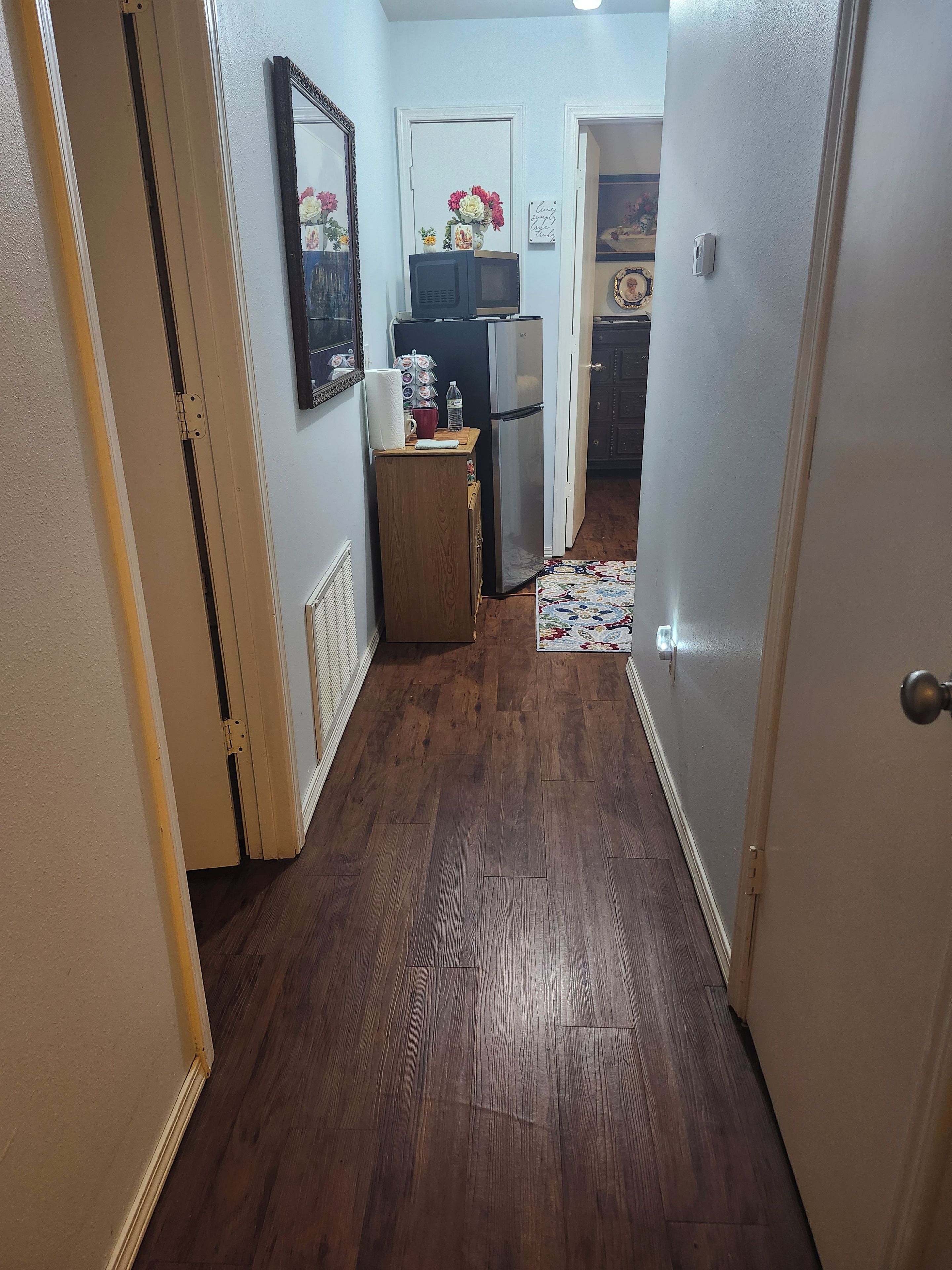 A narrow hallway with wooden flooring leading to a kitchen area.