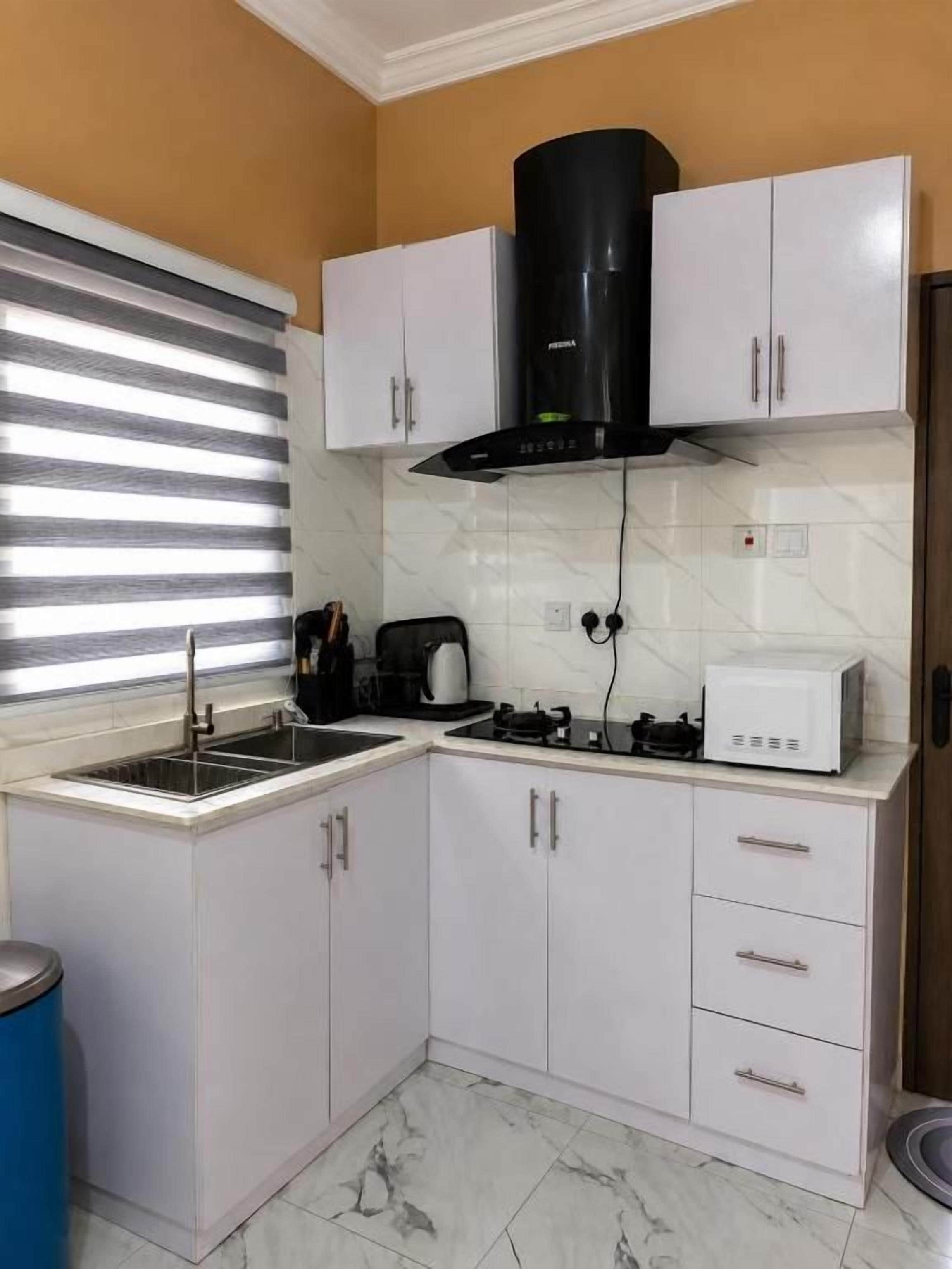 Cocina con armarios blancos, extractor de aire negro, un lavamanos y una ventana con persianas.