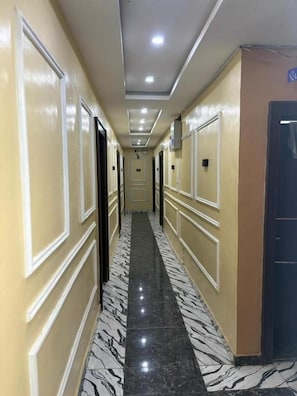 A hotel hallway with a marble floor, cream walls, and doors leading to rooms. - Caligeo Suites II (Ibadan)