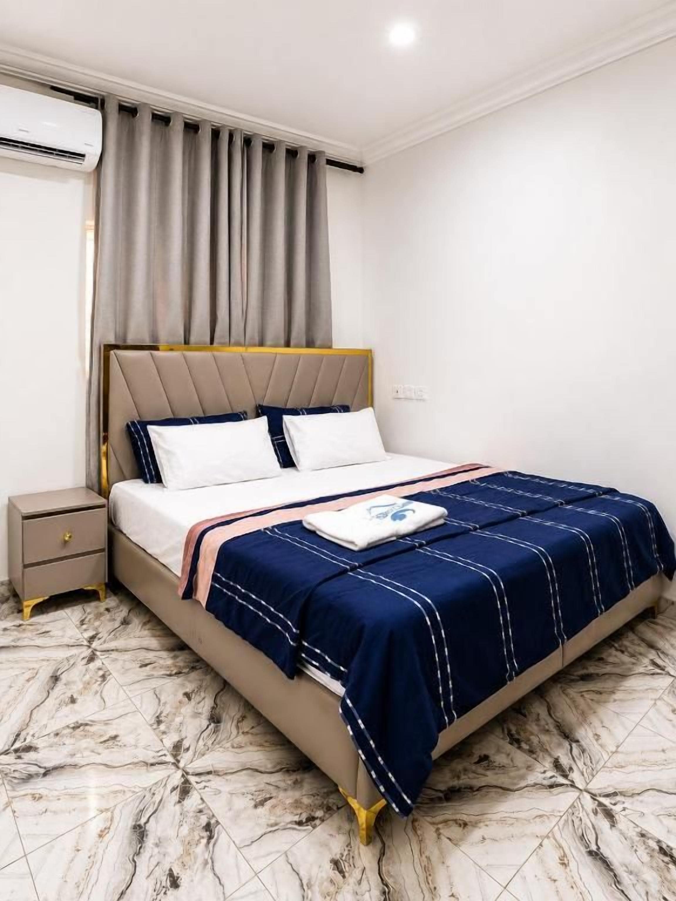 A hotel room with a bed, a nightstand, a wall-mounted air conditioner, and a curtain.