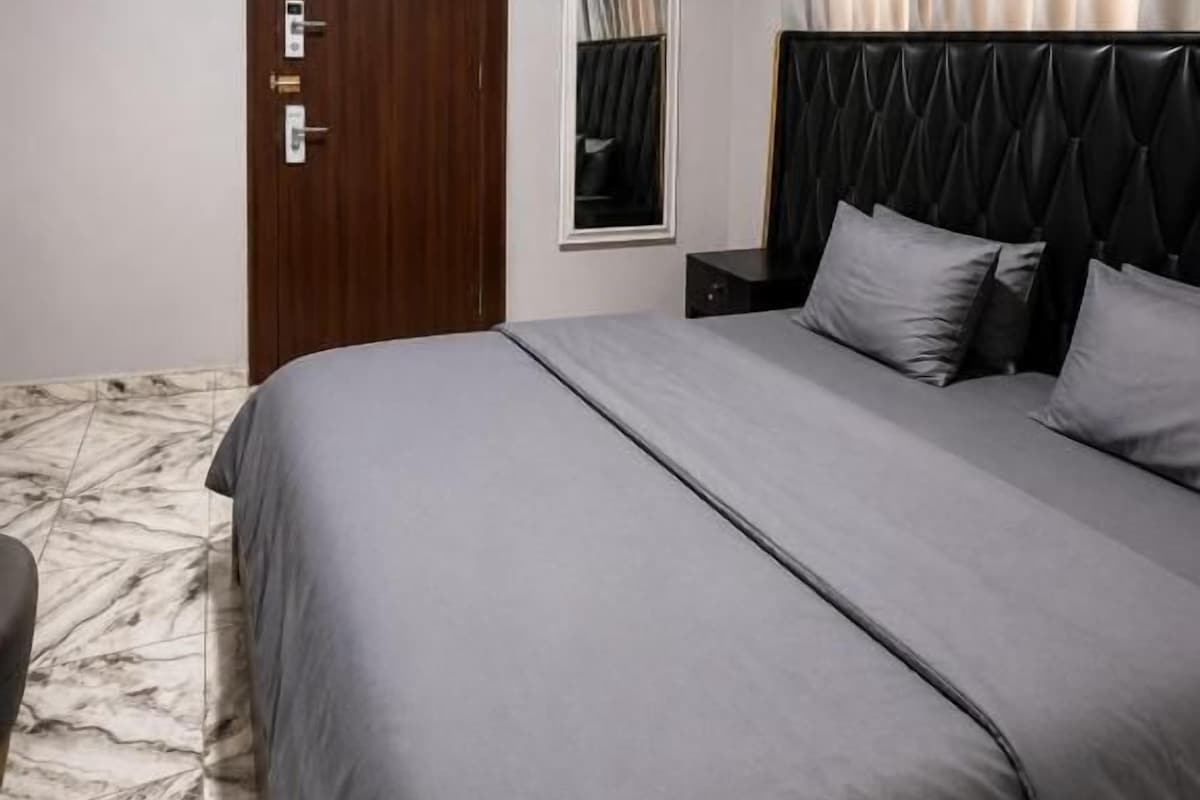 A bedroom with a bed, a door, a nightstand, and a window with curtains.