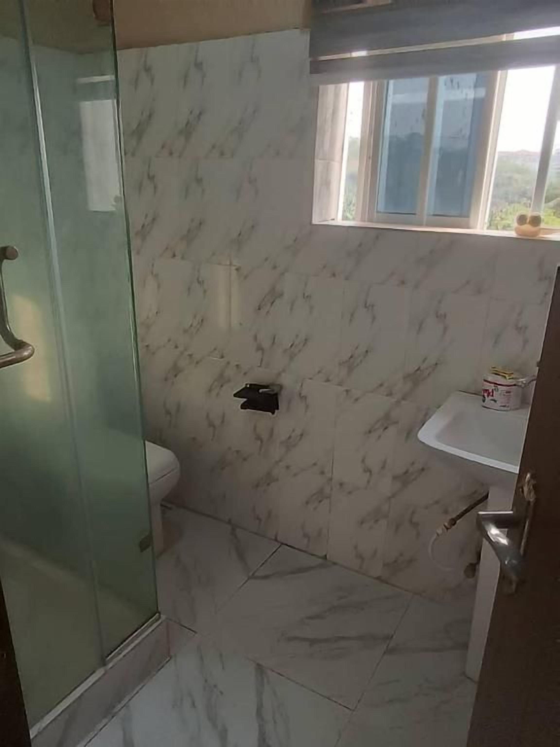 A bathroom with a glass shower enclosure, a toilet, and a small window.