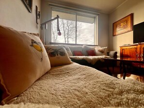 A cozy room with a large window, a bed with decorative pillows, a wooden dresser, and a television. - COZY, WARM, FLEXIBLE, CENTRAL, 2 bedrooms, 2 bathrooms, 3 living areas + parking (Puerto Varas)