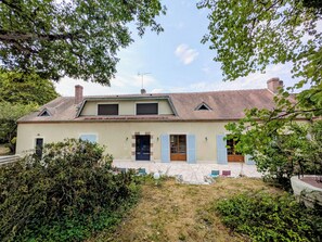A two-story house with a tiled roof, a front door with shutters, and a small garden area with a paved walkway. - Family home between the Loire Valley and Sologne (Lailly-en-Val)