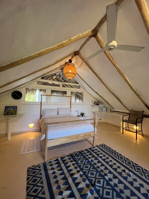 Ein Schlafzimmer im Dachgeschoss mit Bett, Sessel, Pendelleuchte und Deckenventilator.