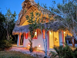 Uma construção com telhado de palha, com interior visível e um caminho de cascalho que a leva.