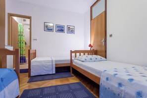 Een kleine, schone kamer met twee eenpersoonsbedden, een houten kast en een deur naar de badkamer. Er hangen drie ingekaderde foto’s aan de muur.