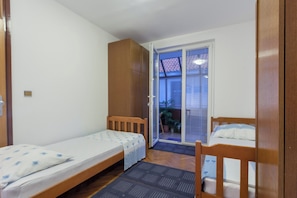 Habitació petita, amb un llit individual, dos llits de fusta, un armari i una porta corredissa de vidre que dona a un balcó.