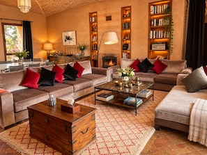A cozy living room with sofas, a coffee table, a fireplace, and bookshelves.