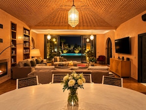 A modern living room with a fireplace, a pool view, and a dining area with a vase of flowers.