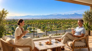 Two people seated on wicker chairs at a table with a view of a cityscape and mountains.