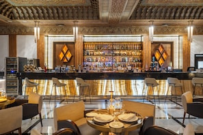 A bar area with a high ceiling and intricate woodwork, featuring a bar counter with a variety of bottles and glasses, and seating with tables set for dining.