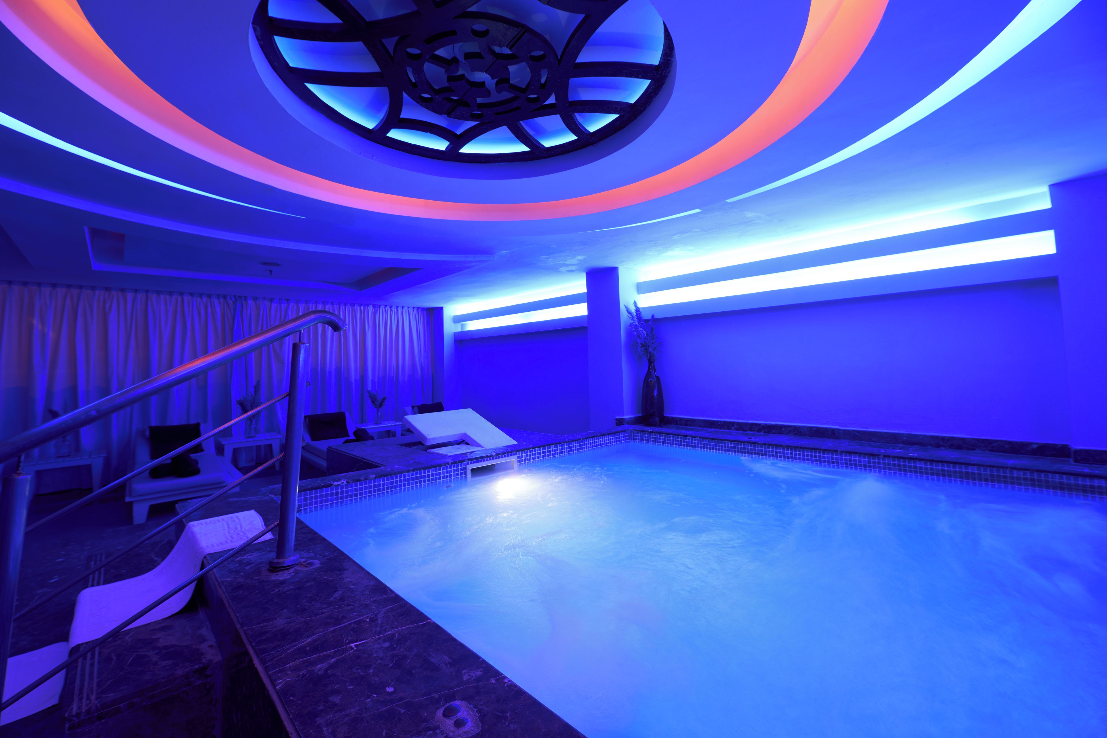Un área de piscina con diseño moderno, que incluye un elemento circular en el techo y una zona de estar con tumbonas.