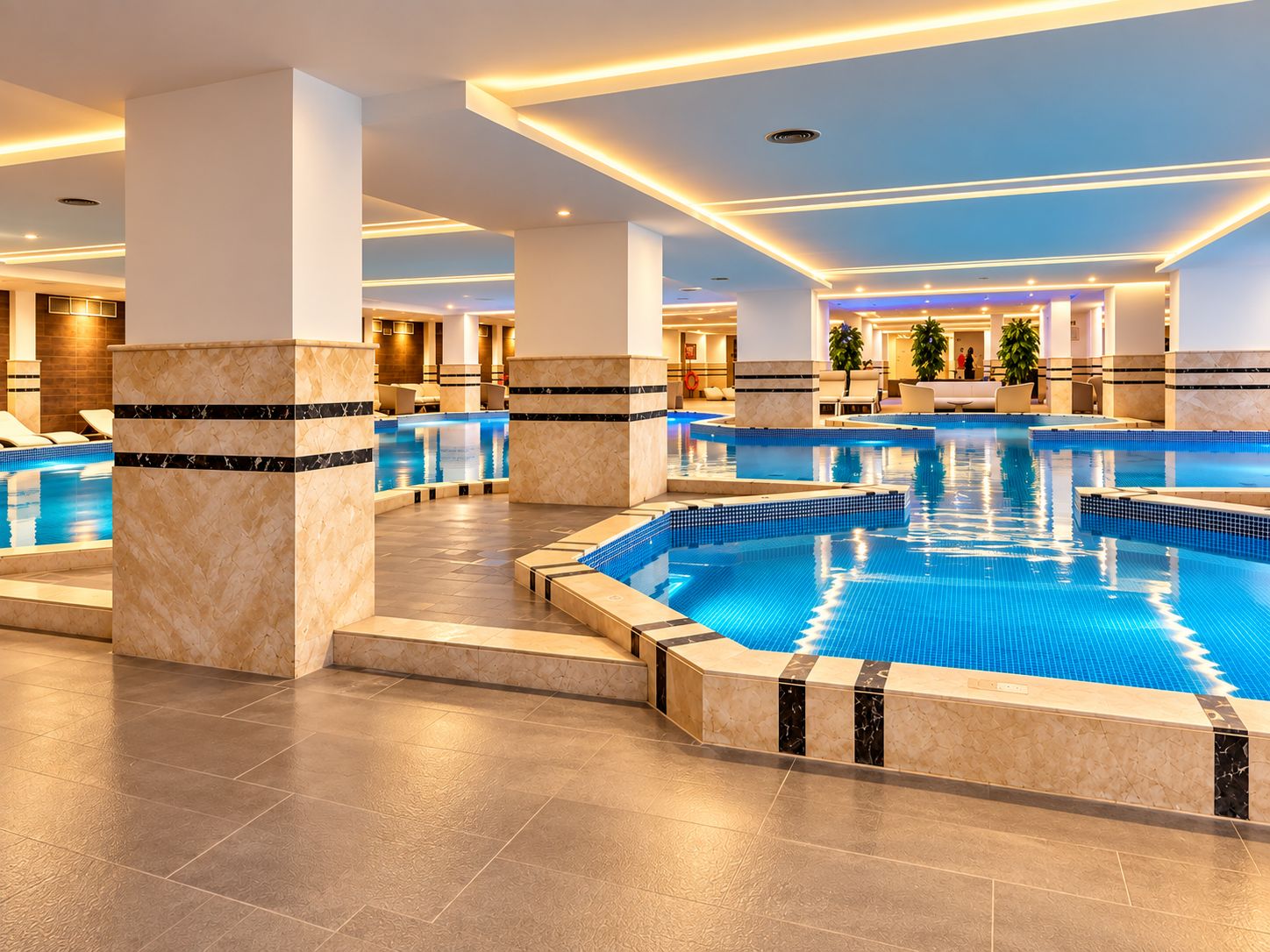 Una amplia piscina cubierta con múltiples carriles, rodeada de zonas de estar y un diseño arquitectónico moderno.