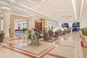 A spacious lobby with a high ceiling, marble flooring, and a central floral arrangement.