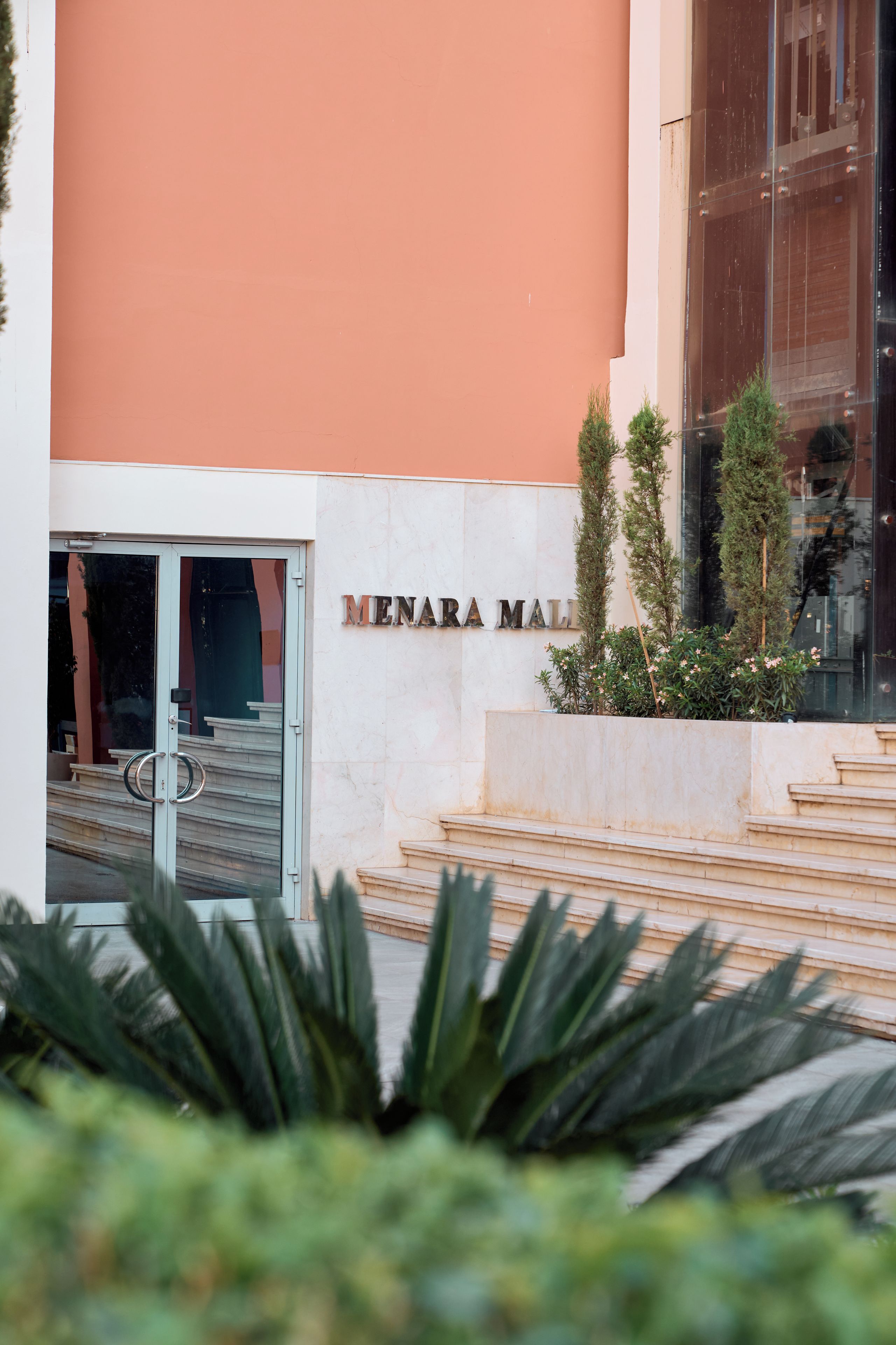 Entrada de un edificio con un cartel que dice 'MENARA MALI' y un conjunto de escaleras que suben a él.
