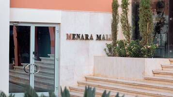 Entrada de un edificio con un cartel que dice 'MENARA MALI' y un conjunto de escaleras que suben a él.