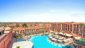 Un resort con una amplia piscina central, varios balcones y un paisaje desértico al fondo.