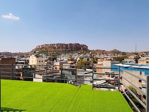 A view of a city with a prominent fort on a hill, surrounded by buildings and a clear sky.