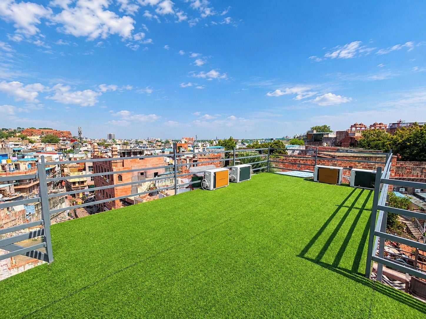 A rooftop with artificial grass, metal railings, and a view of a densely packed urban area.