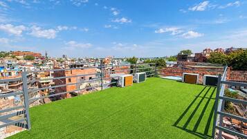 Una azotea con césped artificial, barandillas metálicas y vistas a una zona urbana congestionada.