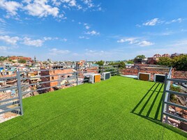 Una azotea con césped artificial, barandillas metálicas y vistas a una zona urbana congestionada.