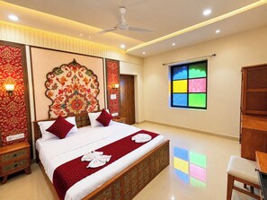 A hotel room with a large bed, a ceiling fan, a window with a colorful view, and a wooden wardrobe.