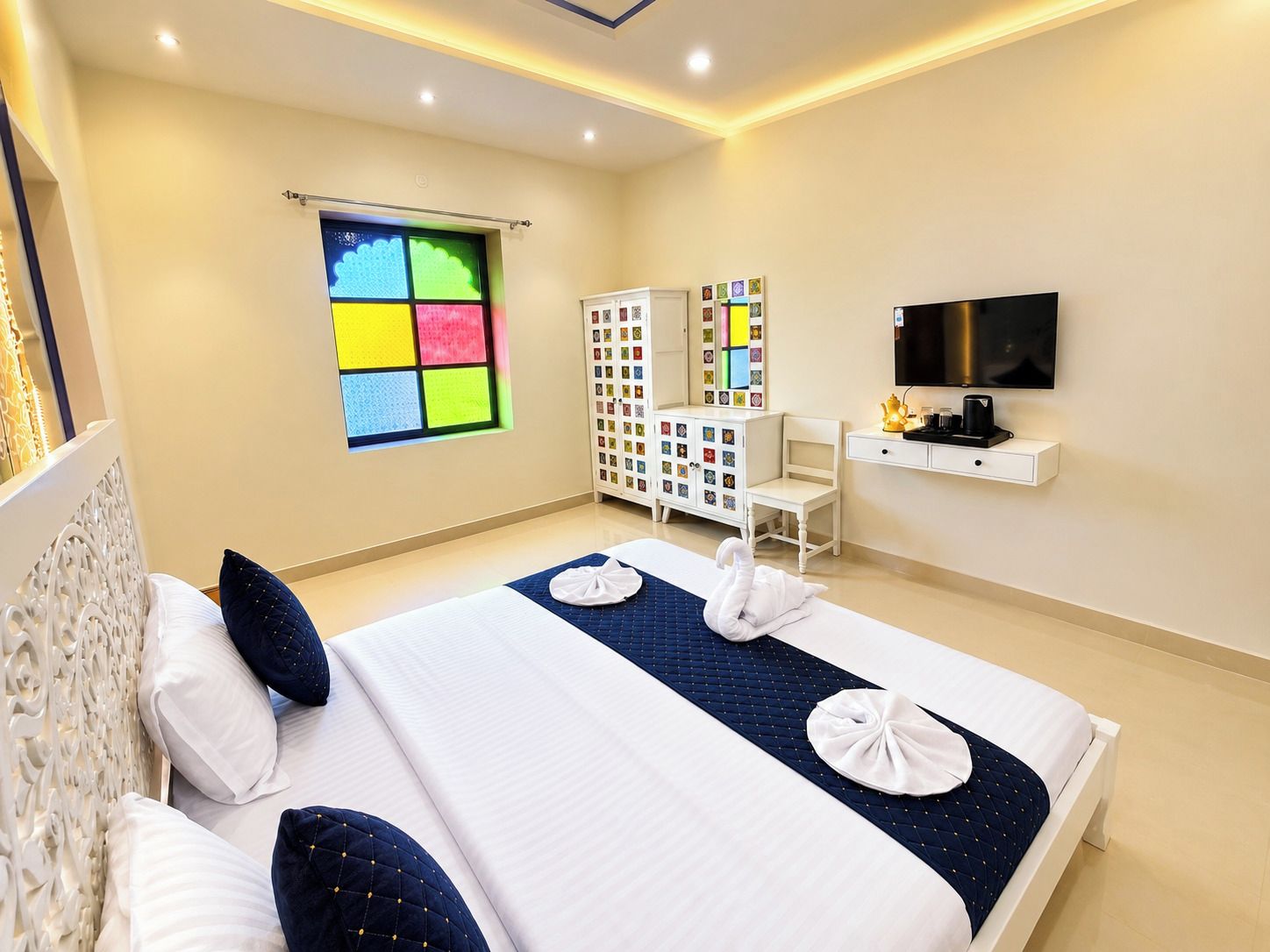 Quarto de hotel com cama, televisão, escrivaninha e armário com fotografias.