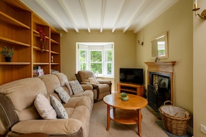 Ein Wohnzimmer mit einer Couch, Sesseln, einem Fernseher, einem Kamin und einem Bücherregal.